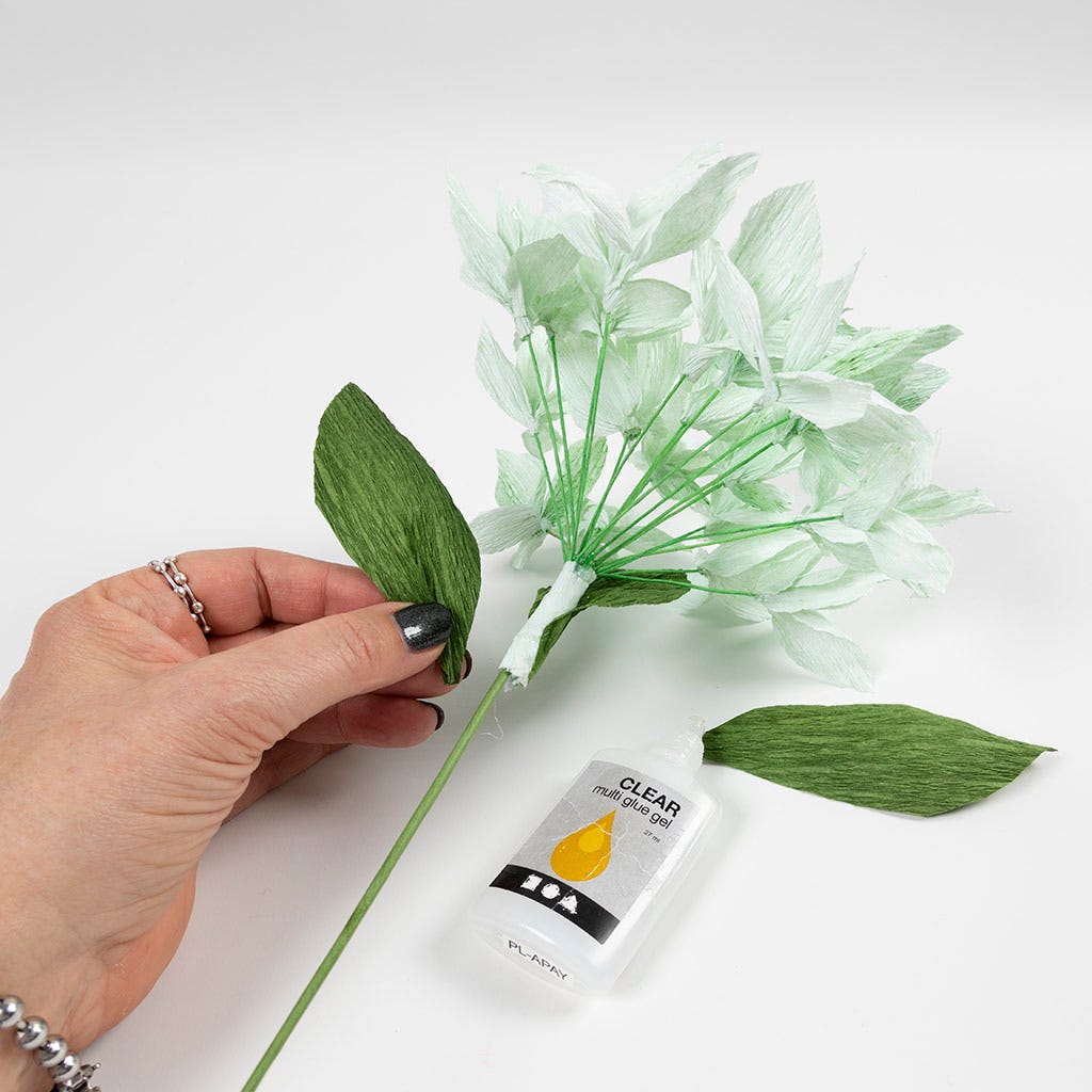Grönt blad av kräppapper fästes på en stjälk med ett stort vitt blomsterknippe